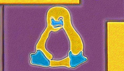 Una imagen macro de Tux, la mascota de Linux, grabado en miniatura en un microprocesador, con un fondo púrpura y detalles en amarillo y azul.